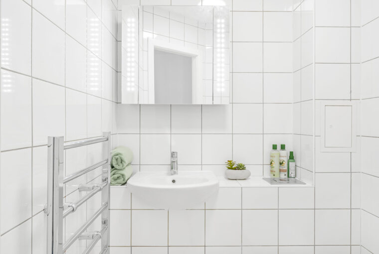 Upclose of sink in a white tiled bathroom with towel drying rack